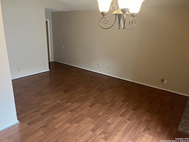 empty room with a chandelier, dark wood-type flooring, a textured ceiling, and baseboards