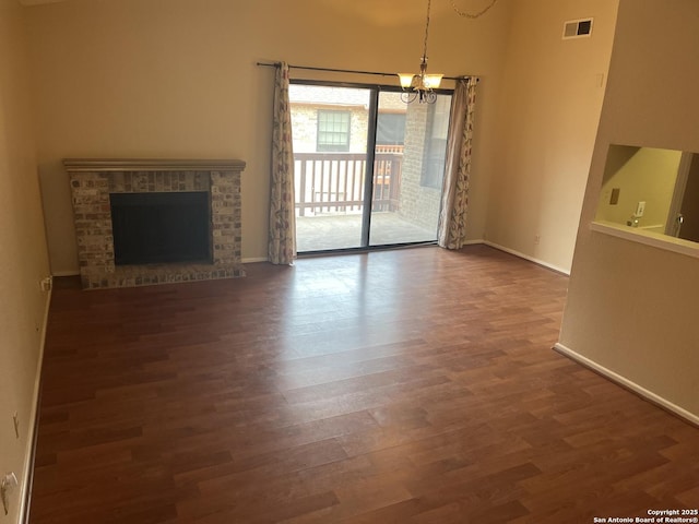 unfurnished living room featuring a notable chandelier, dark wood-style flooring, a fireplace, visible vents, and baseboards