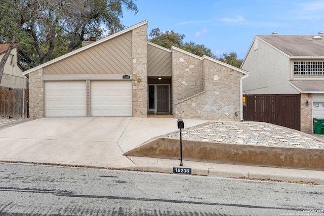 mid-century home with stone siding, driveway, an attached garage, and fence