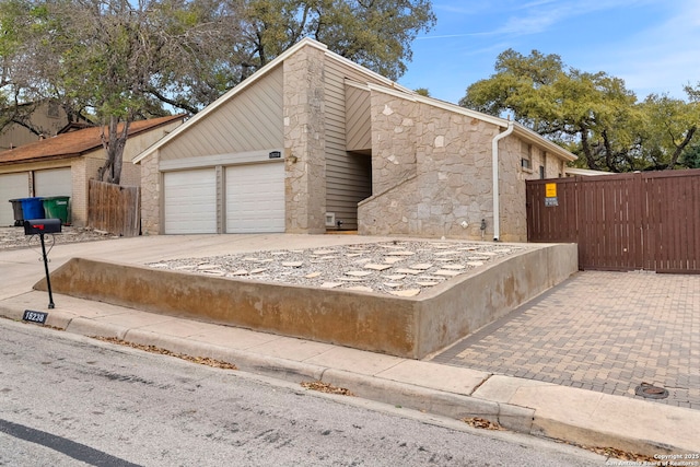 view of front of property featuring a garage, stone siding, driveway, and fence