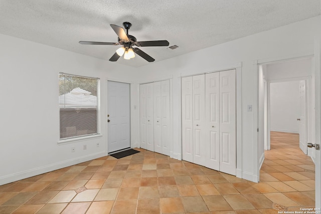 unfurnished bedroom featuring two closets, visible vents, ceiling fan, a textured ceiling, and baseboards