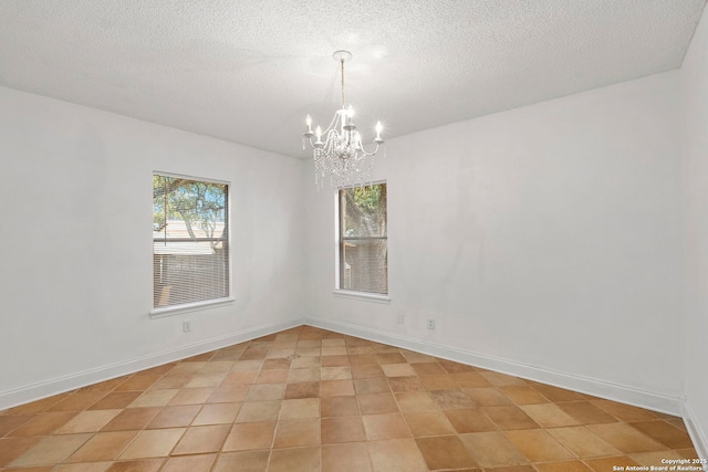 unfurnished room featuring a chandelier, a textured ceiling, and baseboards