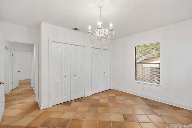 unfurnished bedroom featuring a textured ceiling, baseboards, an inviting chandelier, and multiple closets