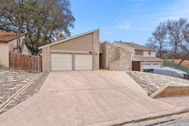 mid-century inspired home with a garage, concrete driveway, stone siding, a chimney, and fence