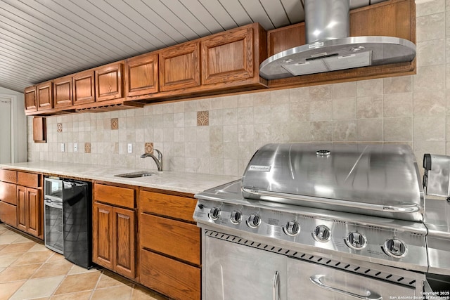 kitchen featuring tasteful backsplash, light countertops, brown cabinetry, a sink, and wall chimney range hood