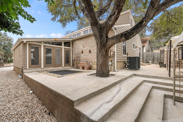 rear view of property featuring stone siding, fence, central AC unit, and a patio