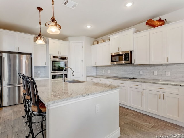 kitchen with stainless steel appliances, visible vents, white cabinets, a kitchen island with sink, and a sink