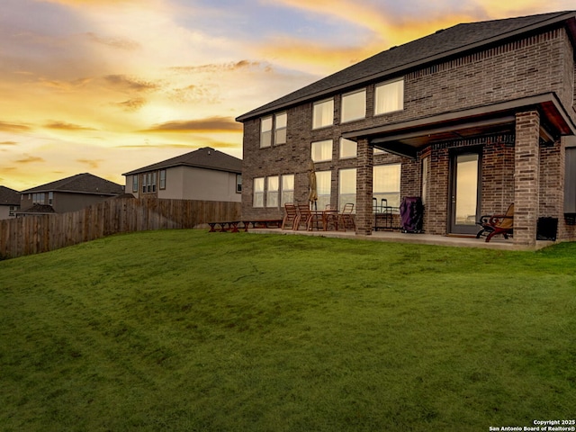 back of house with a patio, brick siding, a lawn, and fence