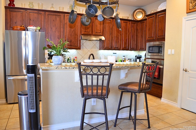 kitchen featuring a breakfast bar area, under cabinet range hood, stainless steel appliances, a center island, and decorative backsplash