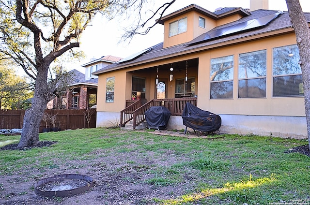 back of property with an outdoor fire pit, a lawn, fence, and roof mounted solar panels