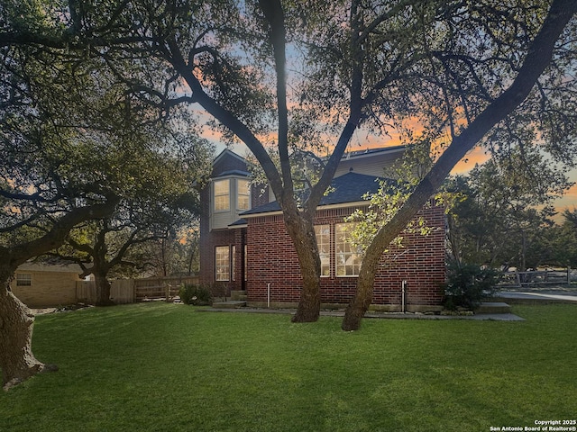 view of front of house featuring brick siding, fence, and a front lawn