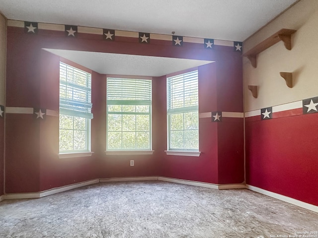 spare room featuring a textured ceiling and baseboards