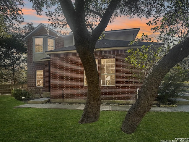 property exterior at dusk featuring a lawn and brick siding