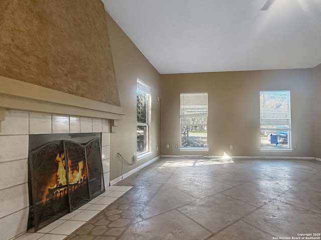 unfurnished living room with a tiled fireplace, plenty of natural light, and baseboards