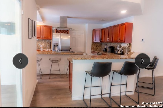 kitchen with a kitchen bar, island exhaust hood, stainless steel refrigerator with ice dispenser, and a peninsula