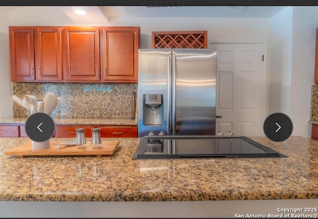 kitchen with light stone counters, tasteful backsplash, stainless steel fridge, and black electric cooktop