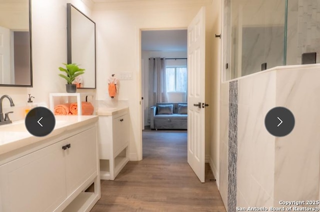 bathroom with a marble finish shower, ensuite bath, two vanities, wood finished floors, and a sink