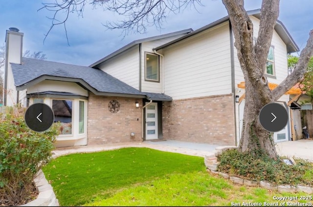 back of house with brick siding, a yard, a chimney, a patio area, and a garage