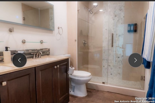 bathroom featuring double vanity, toilet, a stall shower, a sink, and wood finished floors