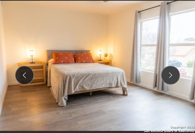 bedroom with multiple windows, wood finished floors, and baseboards