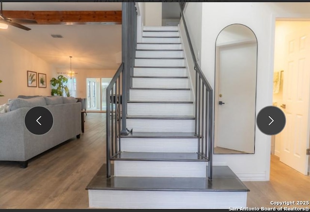 stairs featuring lofted ceiling with beams, baseboards, wood finished floors, and ceiling fan with notable chandelier