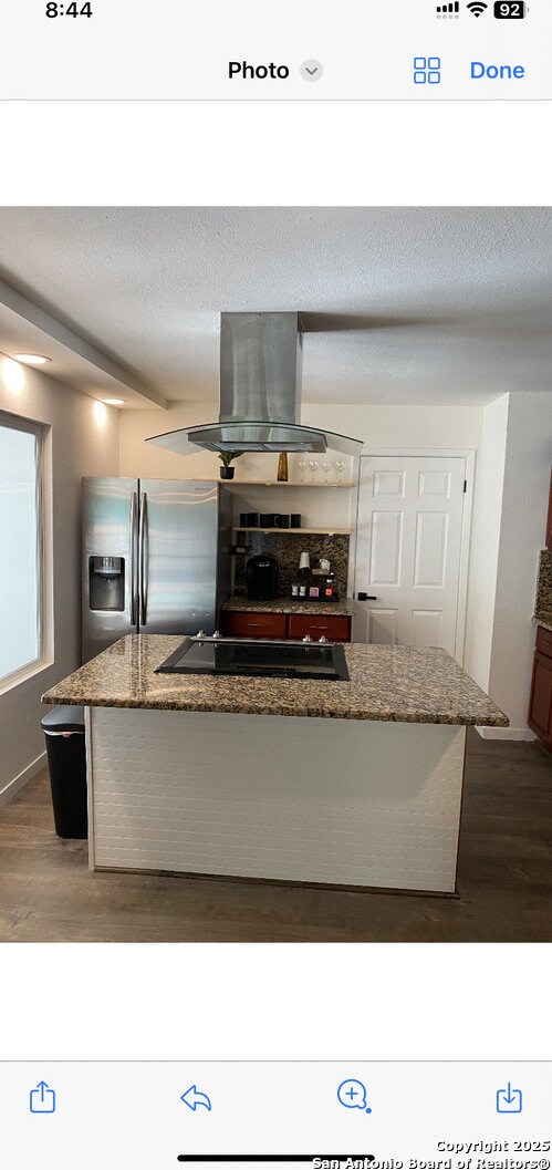 kitchen with black electric cooktop, dark wood-style floors, island range hood, and stainless steel refrigerator with ice dispenser