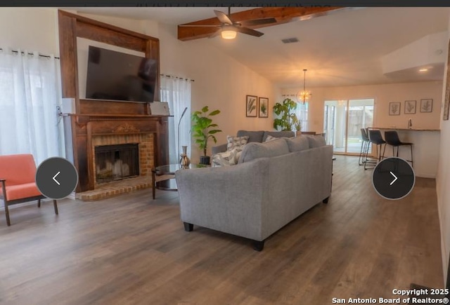 living area featuring vaulted ceiling, a fireplace, wood finished floors, and visible vents