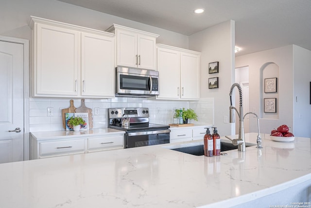 kitchen with light stone counters, stainless steel appliances, recessed lighting, tasteful backsplash, and white cabinets