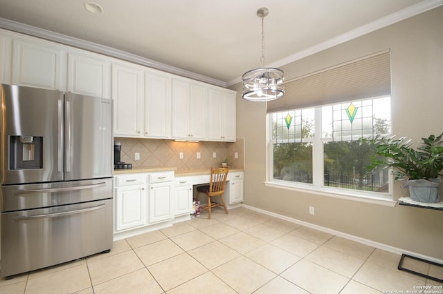 kitchen with built in desk, light countertops, ornamental molding, white cabinets, and stainless steel fridge