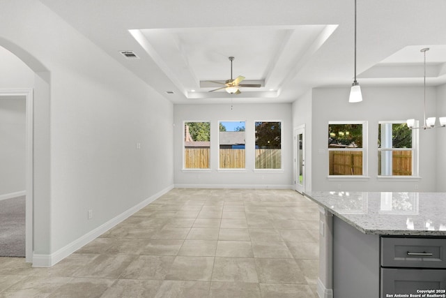 unfurnished living room featuring ceiling fan with notable chandelier, arched walkways, a raised ceiling, and baseboards