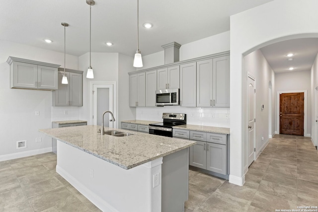 kitchen with light stone counters, stainless steel appliances, tasteful backsplash, a sink, and an island with sink