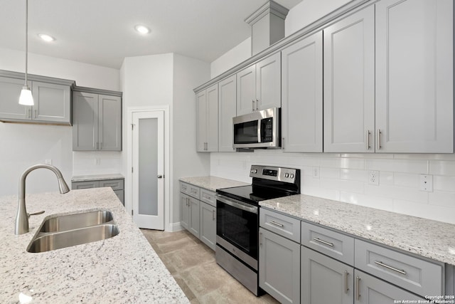 kitchen with light stone counters, a sink, appliances with stainless steel finishes, backsplash, and pendant lighting