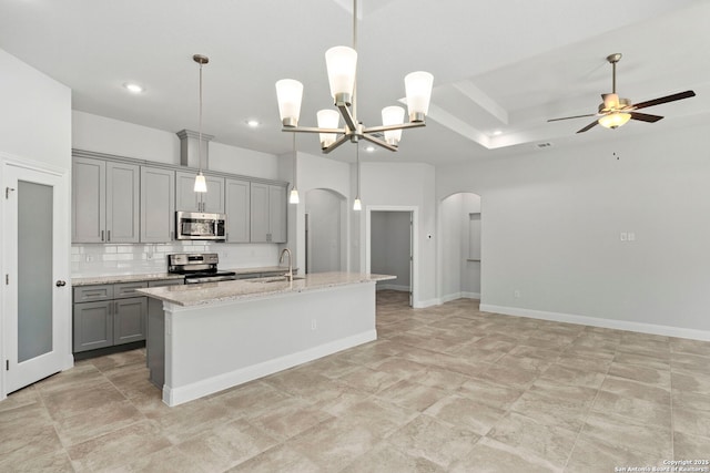 kitchen featuring arched walkways, appliances with stainless steel finishes, an island with sink, and gray cabinetry