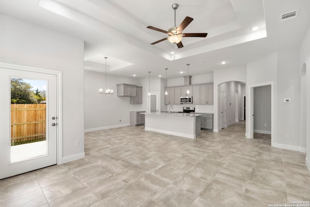 unfurnished living room featuring arched walkways, ceiling fan with notable chandelier, visible vents, baseboards, and a tray ceiling