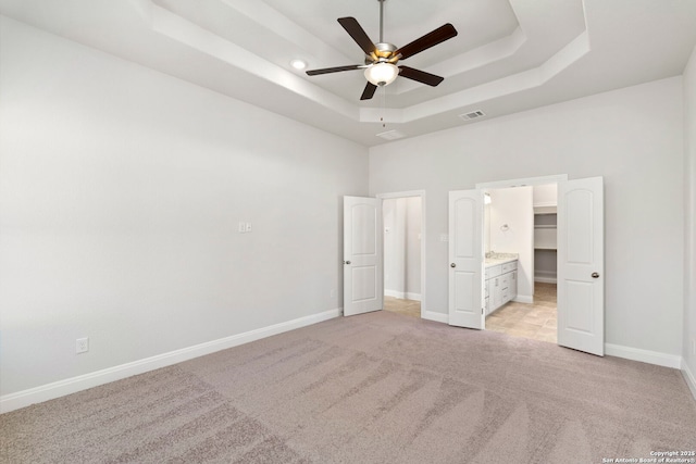 unfurnished bedroom featuring light carpet, baseboards, visible vents, a raised ceiling, and a spacious closet