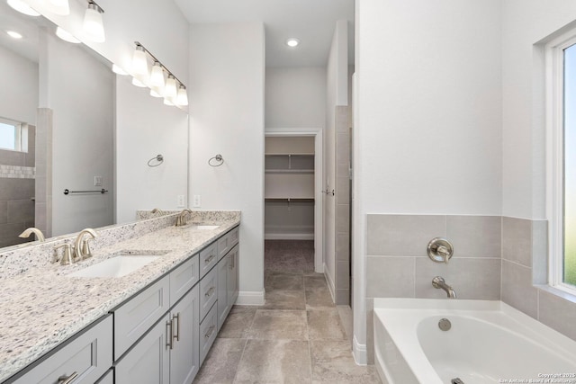 bathroom with a bath, double vanity, a sink, and a walk in closet