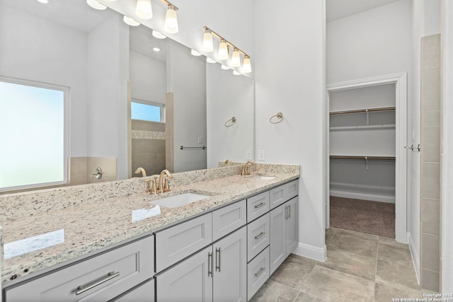 bathroom with a sink, a spacious closet, baseboards, and double vanity