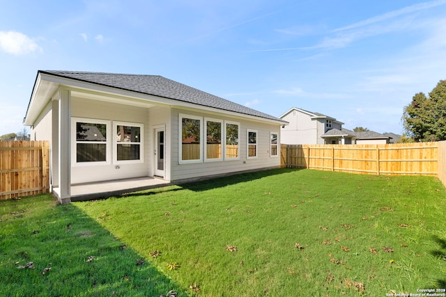 back of property with a yard, a shingled roof, and a fenced backyard