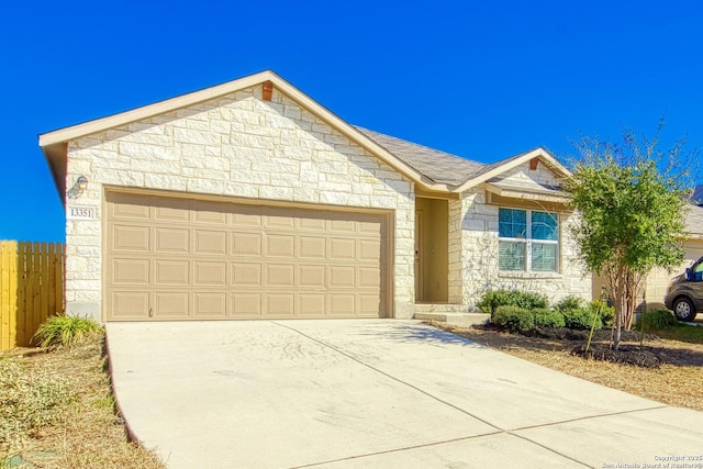 ranch-style home with a shingled roof, concrete driveway, an attached garage, fence, and stone siding