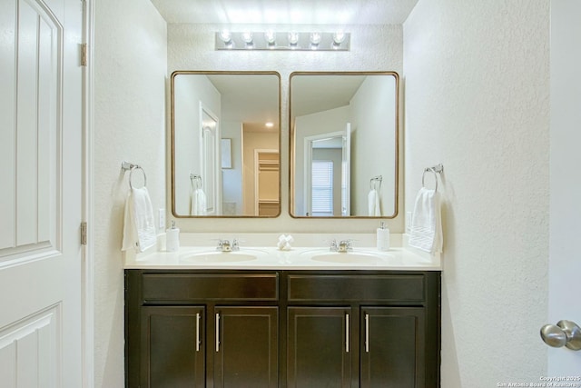 bathroom with a textured wall, double vanity, and a sink