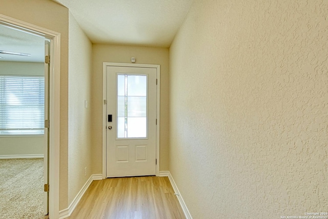 entryway featuring a textured wall, light wood-style floors, and baseboards