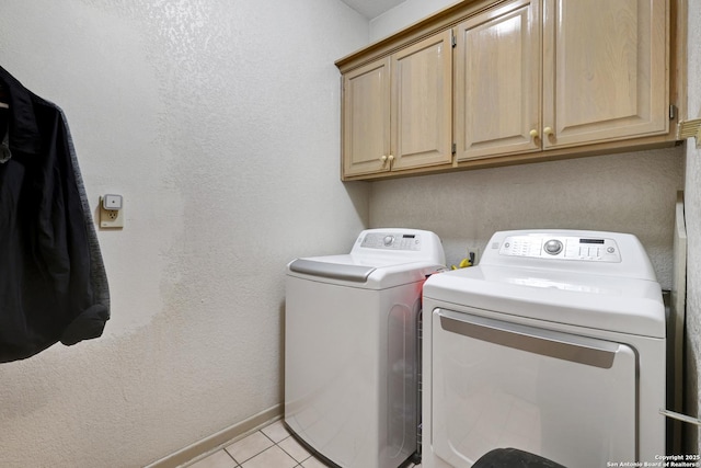 clothes washing area with light tile patterned floors, washing machine and dryer, cabinet space, and baseboards