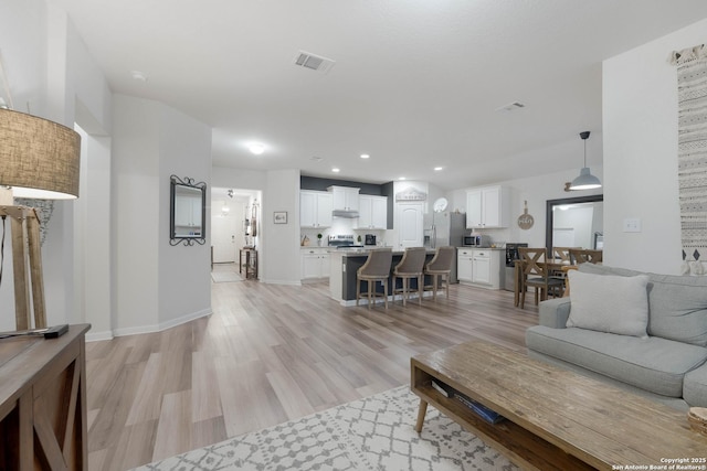 living room with light wood finished floors, visible vents, baseboards, and recessed lighting