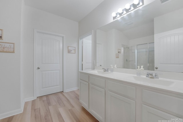 full bath featuring double vanity, a shower stall, a sink, and wood finished floors