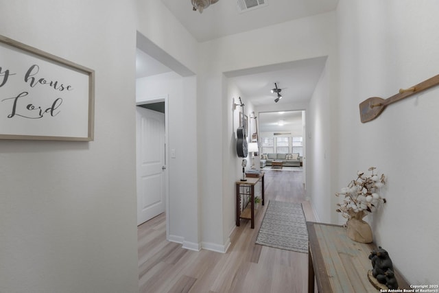 hallway with light wood-type flooring, a barn door, visible vents, and baseboards