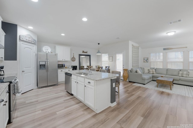 kitchen with visible vents, stainless steel appliances, a kitchen island with sink, and white cabinets