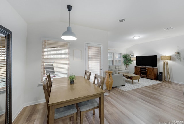 dining space featuring light wood finished floors, baseboards, visible vents, and vaulted ceiling