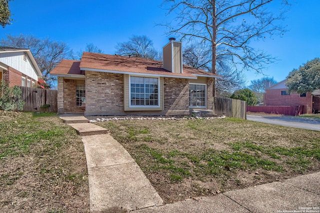 view of front facade with a chimney, fence, a front lawn, and brick siding