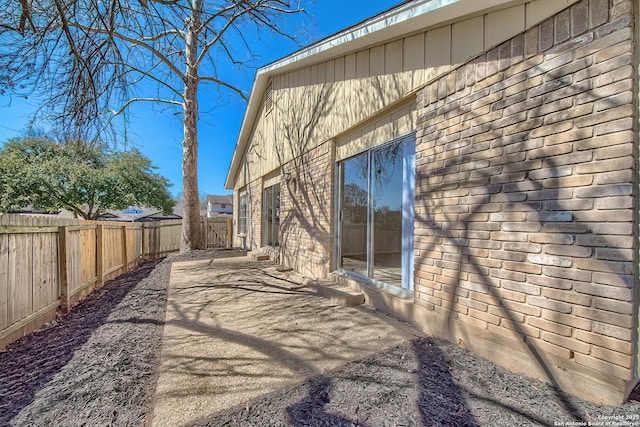 view of side of property featuring a patio, brick siding, and a fenced backyard