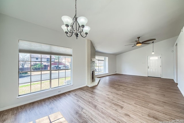 unfurnished living room featuring light wood finished floors, lofted ceiling, a brick fireplace, baseboards, and ceiling fan with notable chandelier